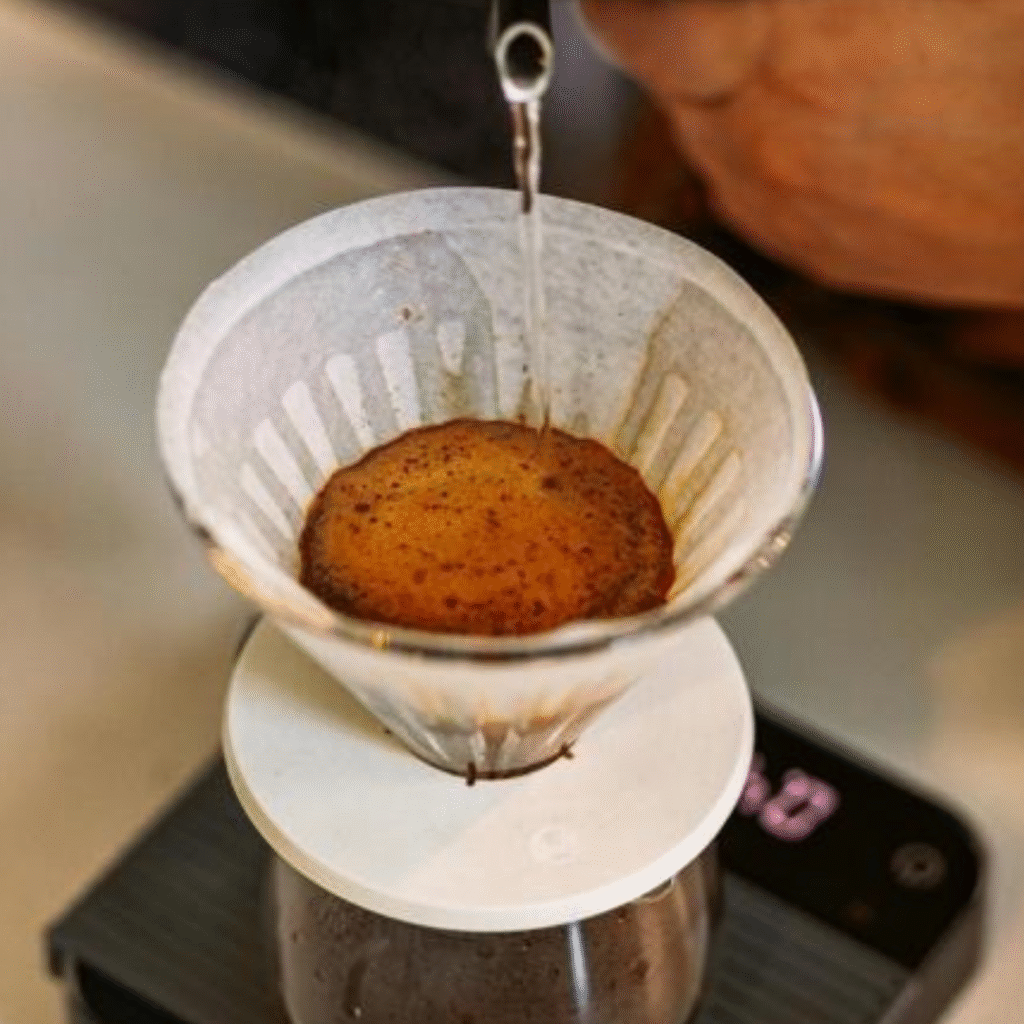 Heet water wordt langzaam over koffie gegoten tijdens het bloomen in een pour-over filter voor ambachtelijke koffie.