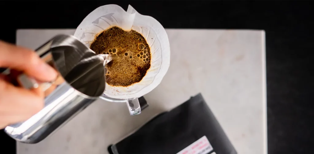 Een foto van een koffiefilter en een kan warm water waarmee een koffie wordt gemaakt